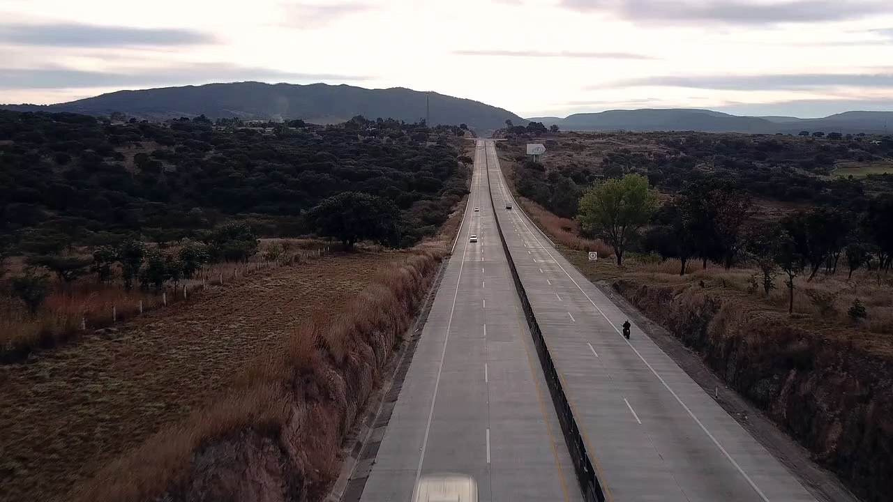 Aerial shot of a motorcycle rider A man riding a motorbike on third street, wearing a helmet and black jacket. Cars pass across the street. The sky was clear in the afternoon, before sunset.