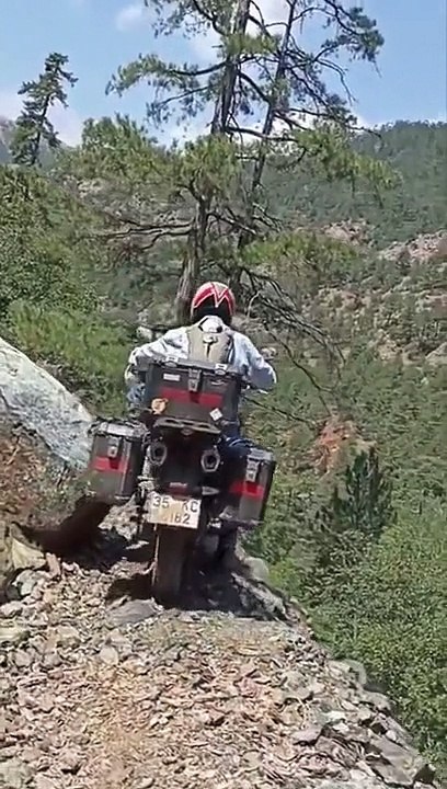 Un motard force pour passer sur un chemin de montagne très étroit