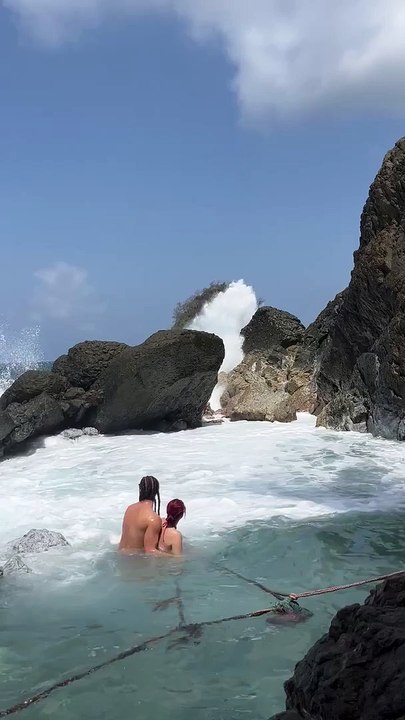 Waves Crash Into Swimmers Resting in Natural Pool