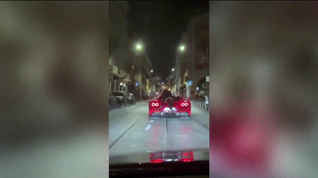 Parla al telefono sul cofano di una Ferrari in movimento, a Milano