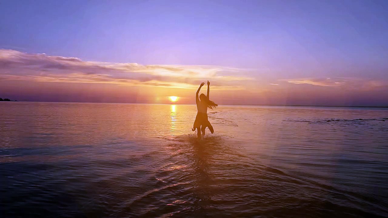 Excited woman running towards the sunset at the seaside