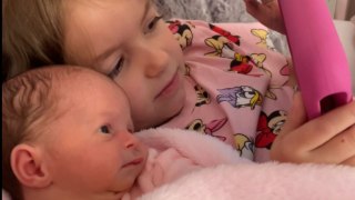 Adorable newborn trying to fight sleep while bonding with her loving big sister