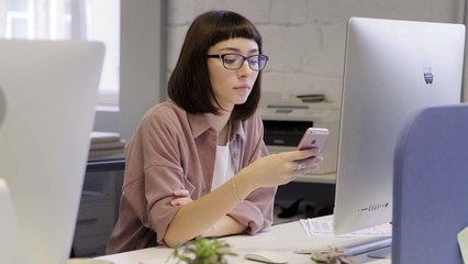 Women using phone in front of computer