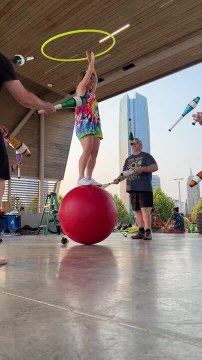 Circus Performer Balances on Ball With Hoop While Men Juggle Pins