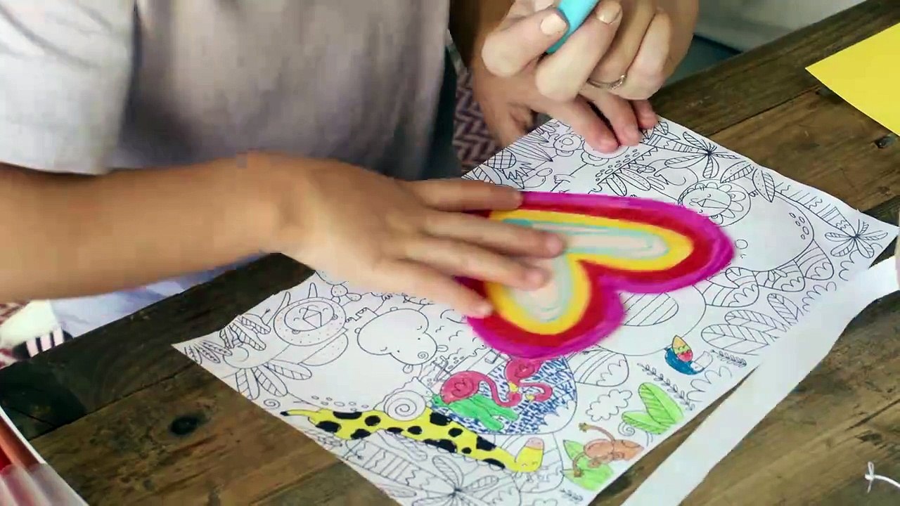 A little girl creating a hand crafted valentine letter with paper and markers on the table