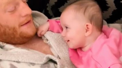 Baby girl smiles sleepily at dad while trying to stay awake