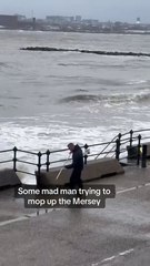 Man is trying to mop up water from waves crashing over the wall!