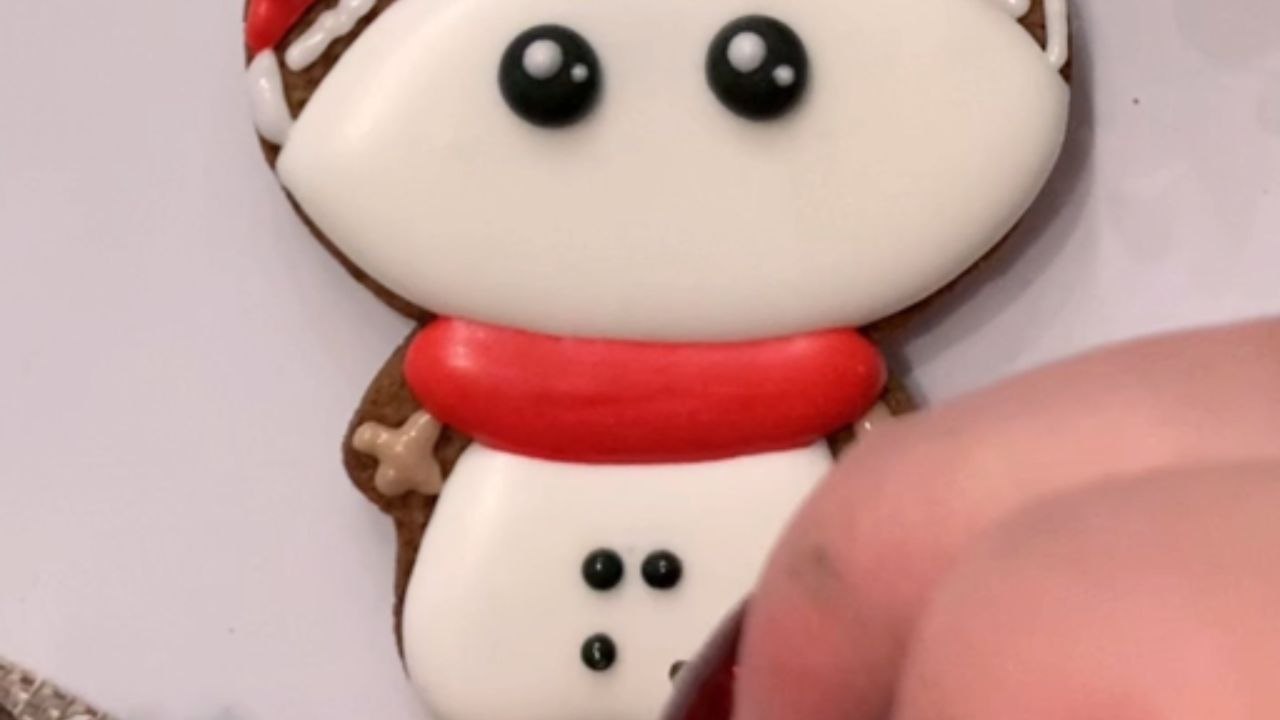 Woman decorates snowman cookie with royal icing...