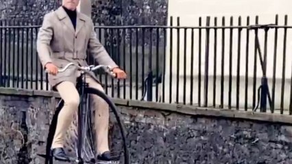 Man rides a vintage high wheeler through the street like a time traveler
