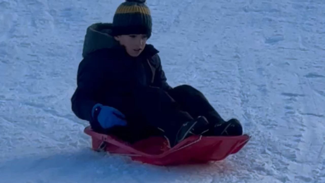 Tiny tot glides down a snow-covered slope on his sled like a pro