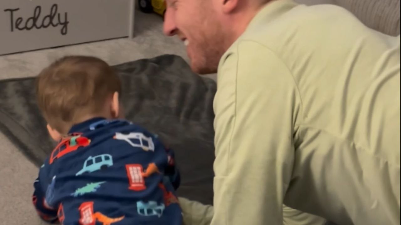 Tiny tot keeps sitting on the blanket while dad tries rolling it up