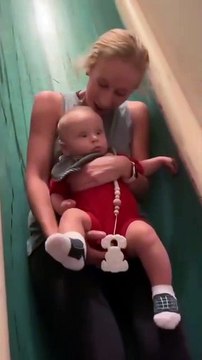 A woman goes down a house slide and asks her baby if he likes it. The camera zooms in on the baby as he stares with wide eyes. How was that