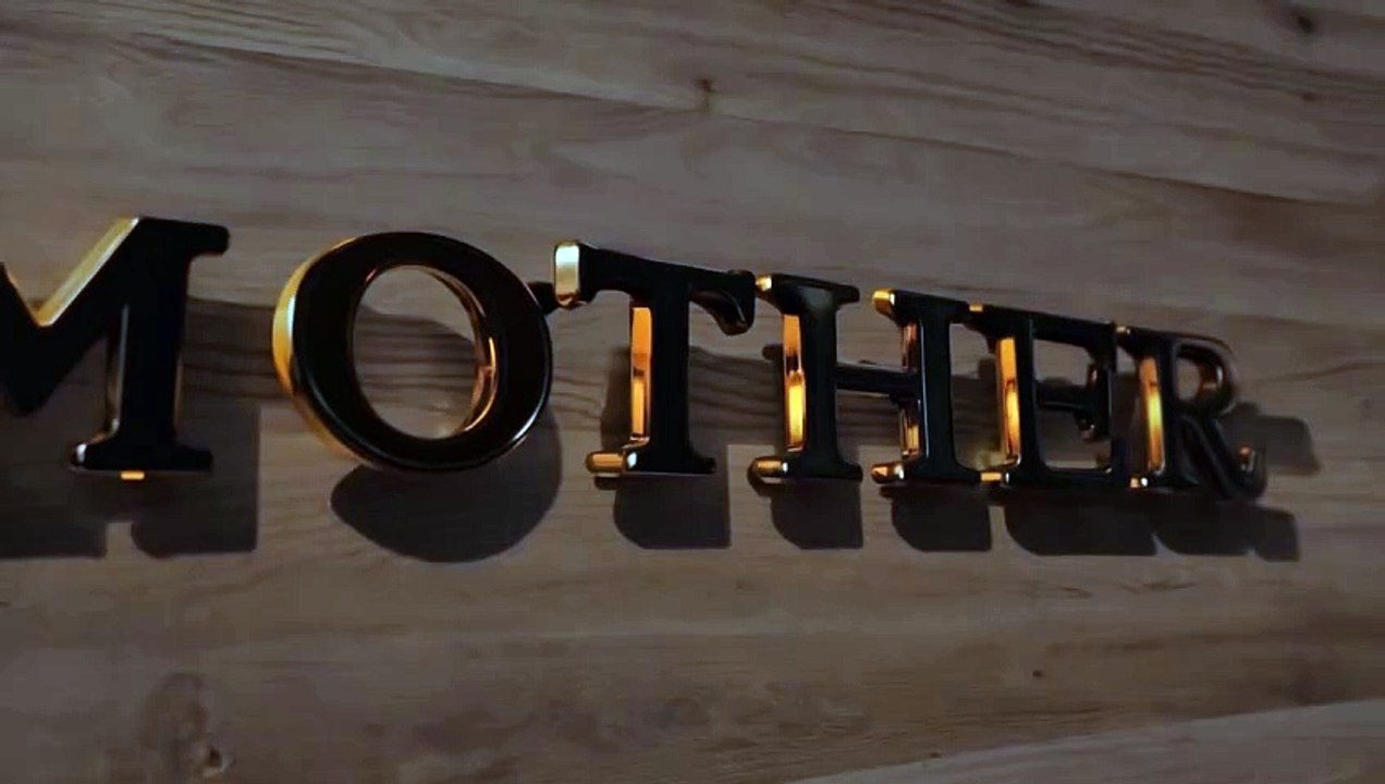 Close-up video of the word "MOTHER" spelled out in black and gold 3D letters, mounted on a wooden surface. The camera pans slowly across the letters, highlighting their details and textures.