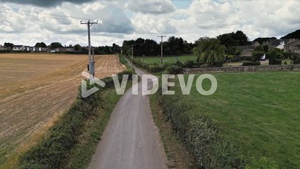 Rural aerial scene with a tractor driving down a country lane, surrounded by fields and farmland