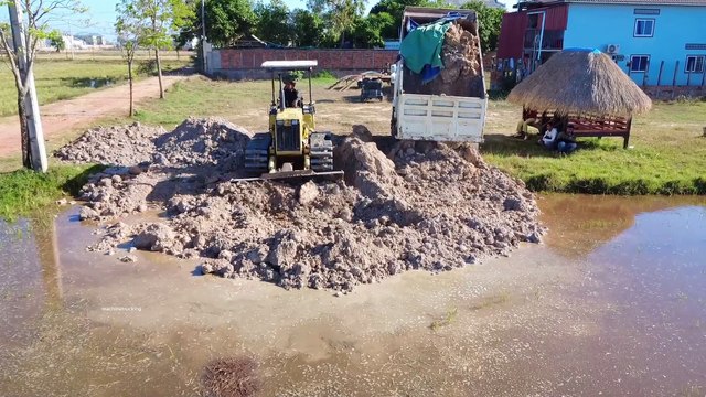 The action of Komatsu bulldozer pushing soil into water with dump truck transport soil