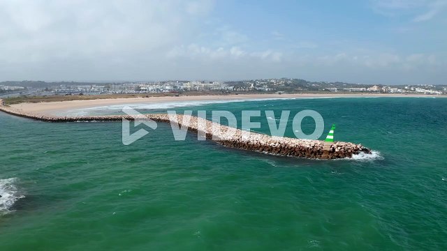 Aerial view of breakwater structure in Lagos coastline, Algarve, Portugal, drone circling around above windy sea, day