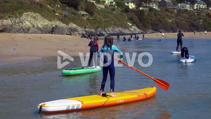 Children paddleboard on a Cornish beach in gentle water