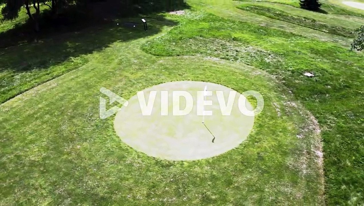 Circular putting green and golf course hole with windblown flag, drone
