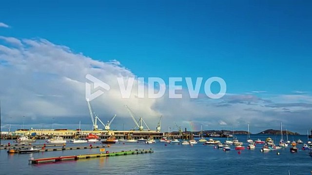 Time lapse of boats sailing industrial shipping port at day time while rainbow appears in clouds