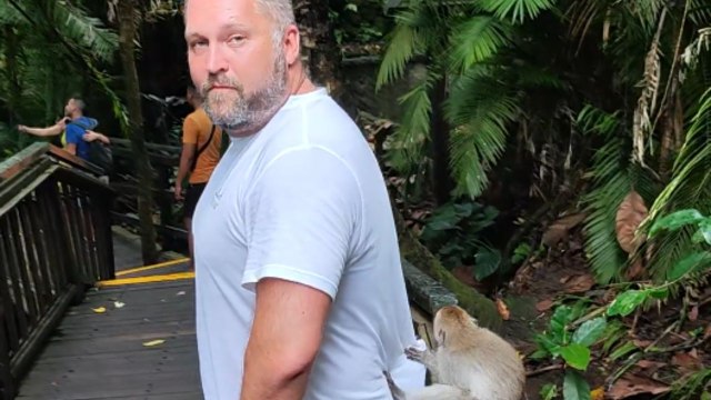 Playful monkey grabs and tries to bite a girl's finger at a busy tourist spot in Bali