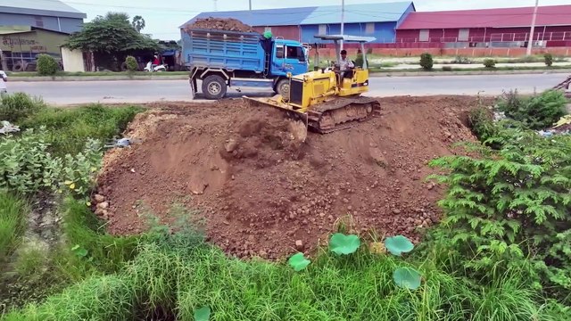 5T Trucks carrying large rocks fill a large hole near a road in Borey