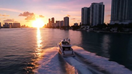 an elegant drone shot of modern boat driving full speed towards the sunset with Miami skylines in the background