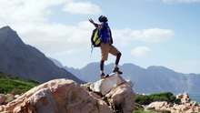 african american man standing on rock with arms wide open while trekking in the mountains
