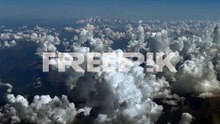 an elevated aerial view from a jet cockpit while flying over cottony cumulus clouds over the alps mountains, with the mont blanc peak in the distance. a cockpit view in a hazy summer morning.