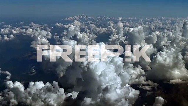 an elevated aerial view from a jet cockpit while flying over cottony cumulus clouds over the alps mountains, with the mont blanc peak in the distance. a cockpit view in a hazy summer morning.