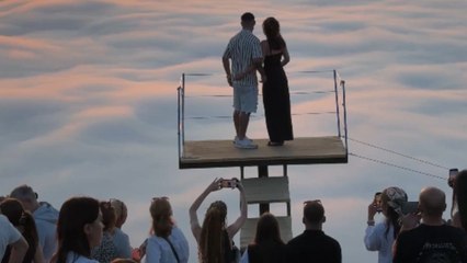 Boy poses a  question to his sweetheart under clouds and sunlit sky