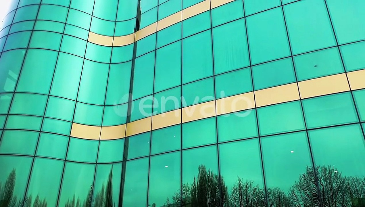 Aerial shot of modern office building windows reflecting cityscape on a sunny day.
