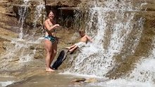 Unexpected hilarity unfolds as woman slips into water while posing for photo near a waterfall