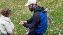 Little girl feeds a squirrel with the help of a family friend