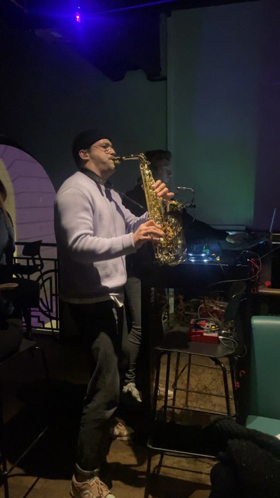 A man plays the saxophone in a cozy bar filled with soft, dim lighting and colorful LED glows. The smooth jazz melody blends with the relaxed, intimate atmosphere. 🎷✨