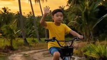 A young boy rides a bicycle along a peaceful village road during sunset, with golden light casting long shadows. Coconut trees sway gently as birds return to their nests. The