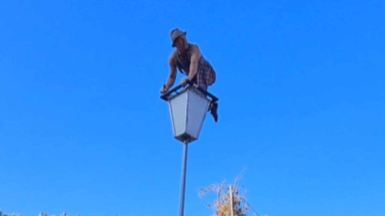 Street performer swings flexible, large pole while standing on top of it